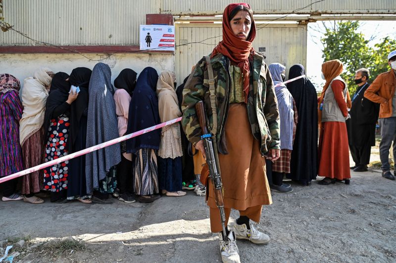 A Taliban fighter stands guard as women wait in line for food from the World Food Programme in Kabul on November 6. | Image: HECTOR RETAMAL/AFP via Getty Images